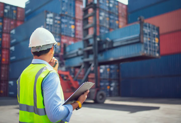 Ein Mann mit Helm und Sicherheitsweste beobachtet die Verladung eines Containers.