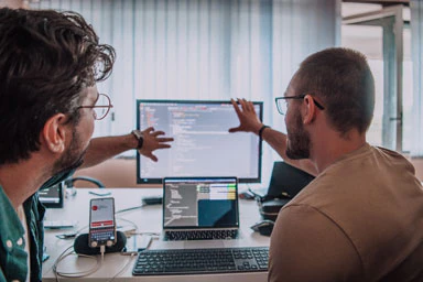 Zwei Männer im Gespräch zeigen auf Dinge auf einem Computerbildschirm.