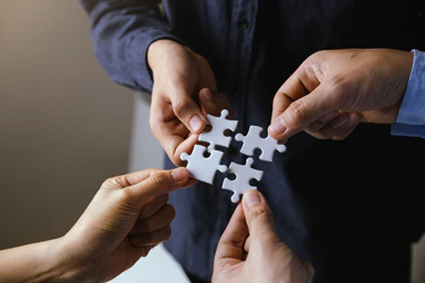 Vier Personen halten je ein Puzzleteil in der Hand.