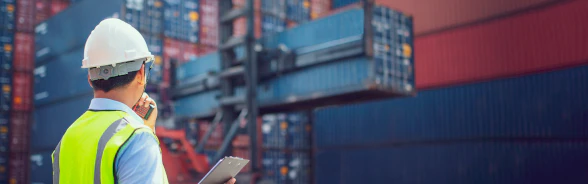 Ein Mann mit Helm und Sicherheitsweste beobachtet die Verladung eines Containers.