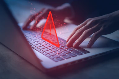 Eine Person am Computer und ein Gefahrensymbol.