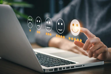 Eine Person vor einem Computer klickt auf einen Smiley, der volle Zufriedenheit ausdrückt.