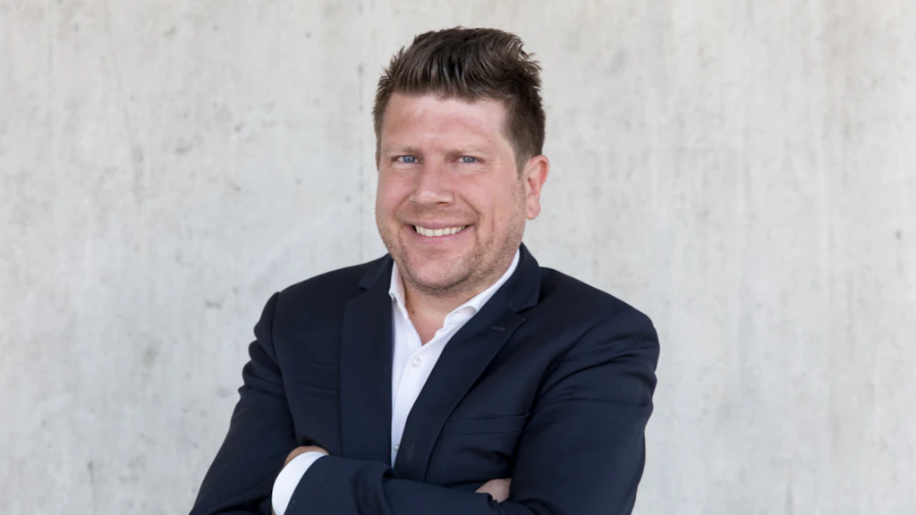 Lächelnder Mann, verschränkte Arme, blauer Anzug, weisses Hemd.