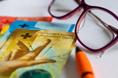 Swiss banknotes, a pair of glasses, and a pen.