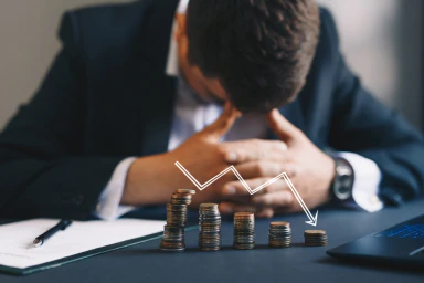 A man with his head down and five stacks of coins with a downward arrow.