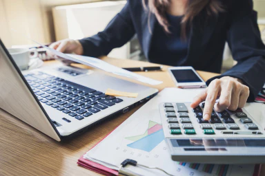 A person sitting at a desk with a computer and a calculator.
