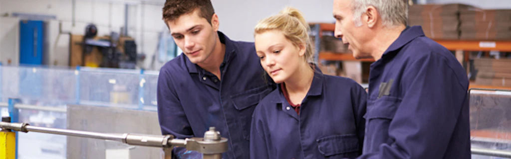 Two apprentices in work clothes listening to an instructor's advice