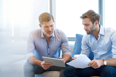 An older man and a younger man discuss while looking at documents.