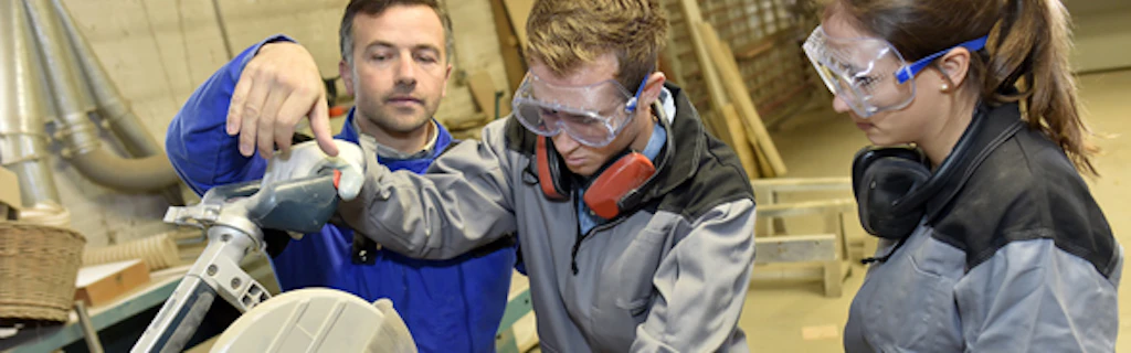 Pair of apprentices making a wooden object, watched by their instructor
