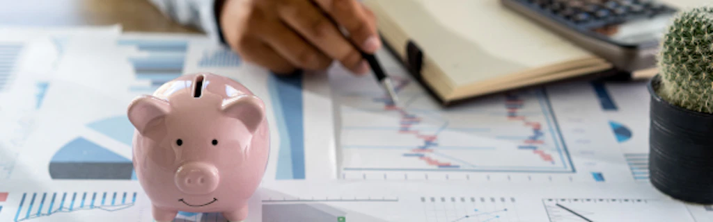 A man performs calculations using a calculator. In the foreground is a piggy bank