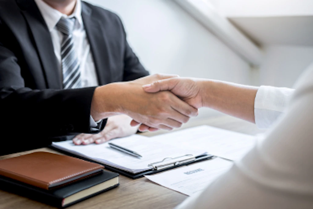 Two people shaking hands across a desk.