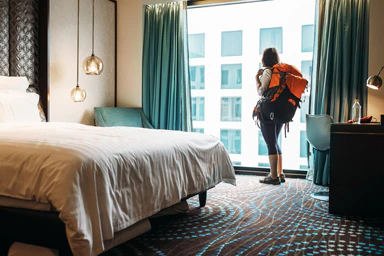 Une femme vue de dos avec un sac de randonnée dans une chambre d’hôtel.