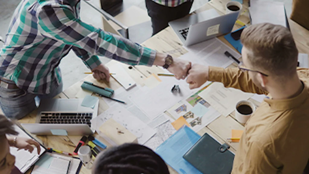 deux jeunes hommes font un check au-dessus de leur table de travail.