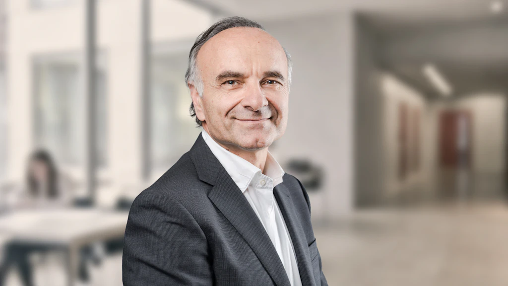 Evangelos Xevelonakis, blazer gris, chemise blanche, homme souriant.
