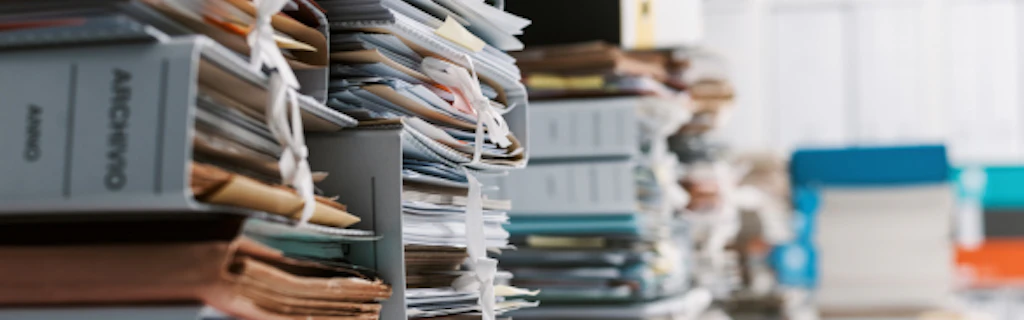 Des classeurs et de documents sont empilés dans un bureau.