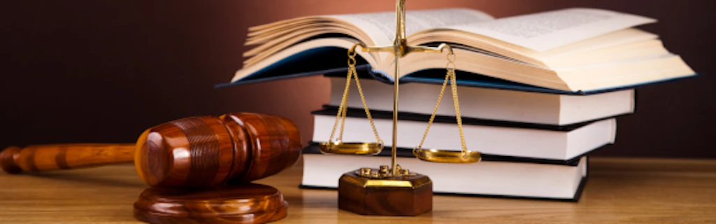Un marteau et une balance sont posés devant un tas d'ouvrages de droit.