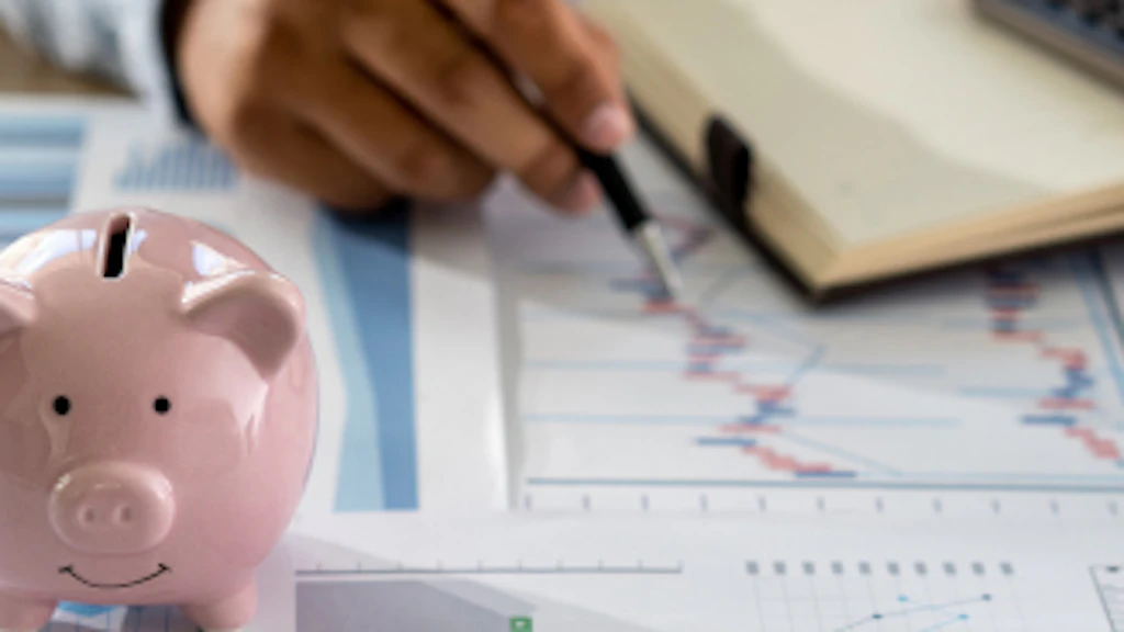 Un homme effectue des calculs à l'aide d'une calculatrice. Au premier plan figure une tirelire en forme de cochon.