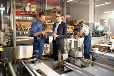 Une dame en habits formels discute avec un employé dans une manufacture.