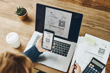 Una persona paga le sue bollette QR con lo smartphone, il computer e la calcolatrice.