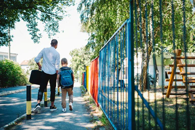 Un uomo accompagna un bambino lungo la strada di scuola.