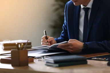 Un uomo in giacca e cravatta firma un documento.