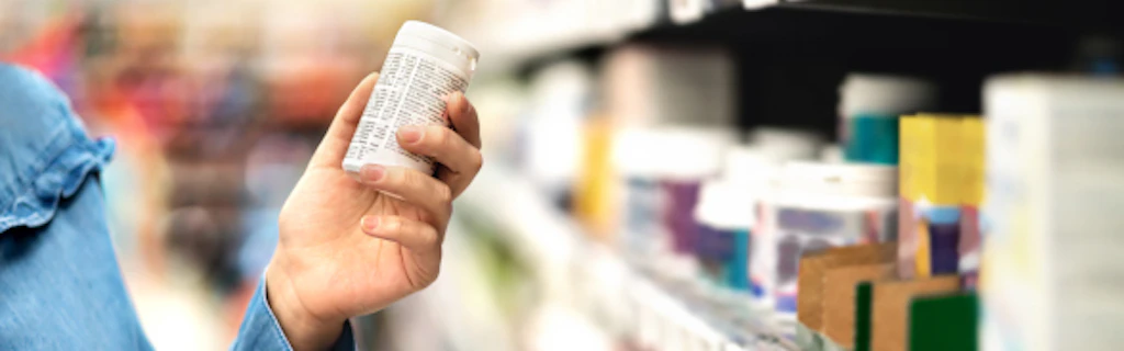 Un consumatore prende una scatola di medicinali dallo scaffale di un negozio.