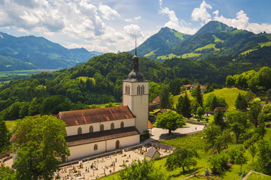 Una chiesa in un paesaggio verdeggiante e circondato da montagne.