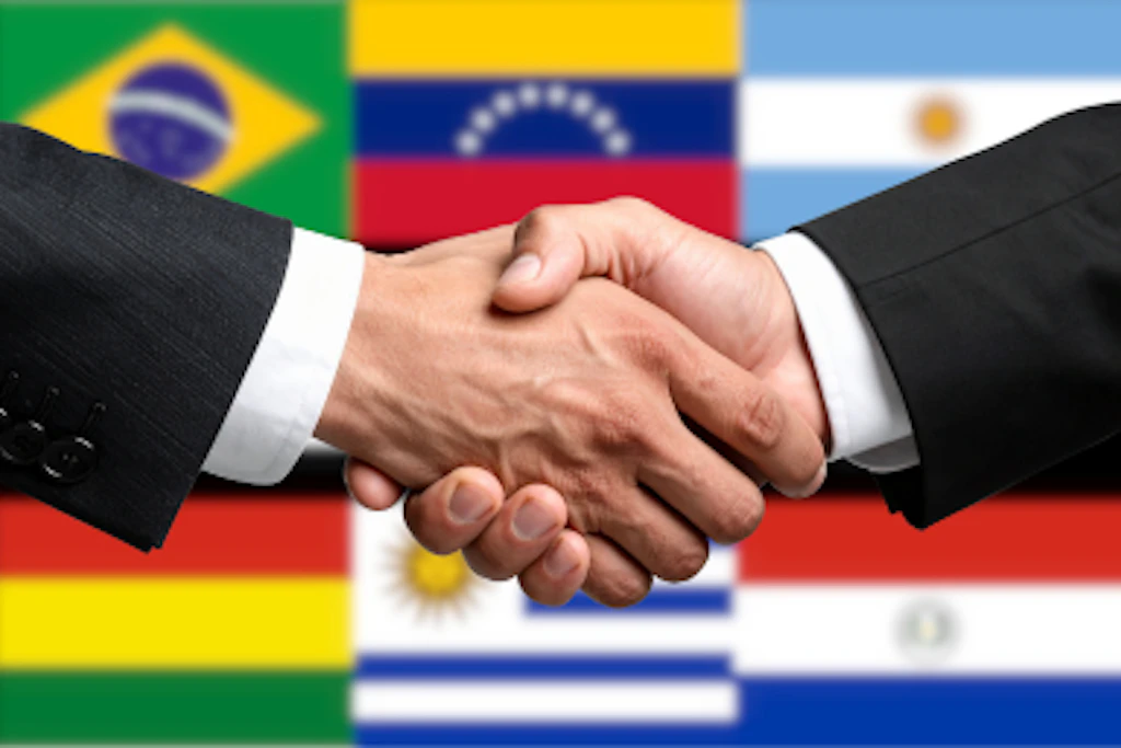 Stretta di mano su sfondo di bandiere dei Paesi membri del Mercosur.